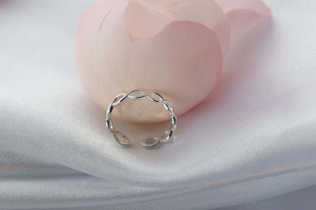 Anillo de plata 925 trenzado con apertura para ajustar talla exhibido sobre seda blanca con pétalo rosa