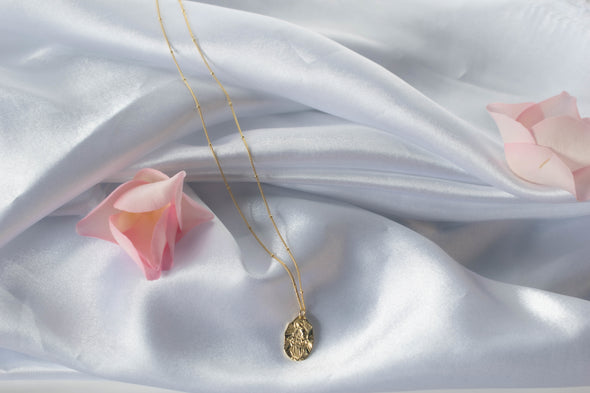 Collar cadena con pendiente de virgen milagrosa color oro sobre superficie seda blanca