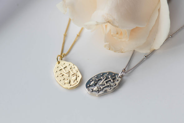 Collar cadena con pendiente de virgen milagrosa color oro y color plata detrás sobre superficie blanca