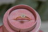 Anillo en baño de oro 18k con Piedra zirconia central e incrustaciones exhibido en caja de joyas rosa