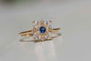 Anillo de plata 925 con baño de oro 18k y piedras centrales en forma de flor de zirconias blancas y azul exhibido sobre una superficie blanca en Guatemala