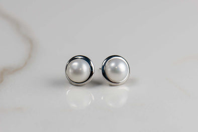 Aretes pequeños de perla con marco plateado liso sobre superficie blanca