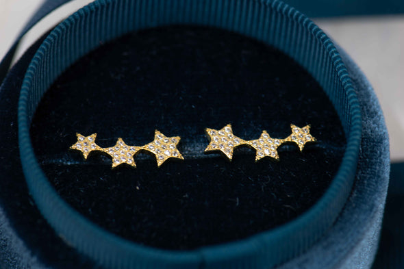 Aretes tipo climbers de estrellas con baño de oro 18k sobre caja de joyas azul