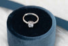 Anillo de plata 925 ajustable con zirconia central grande y zirconias pequeñas incrustadas en la banda exhibido dentro de caja de anillo Negra con azul