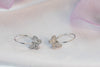 un par de argollas en plata 925 con mariposa colgante con zirconias exhibido sobre superficie blanca