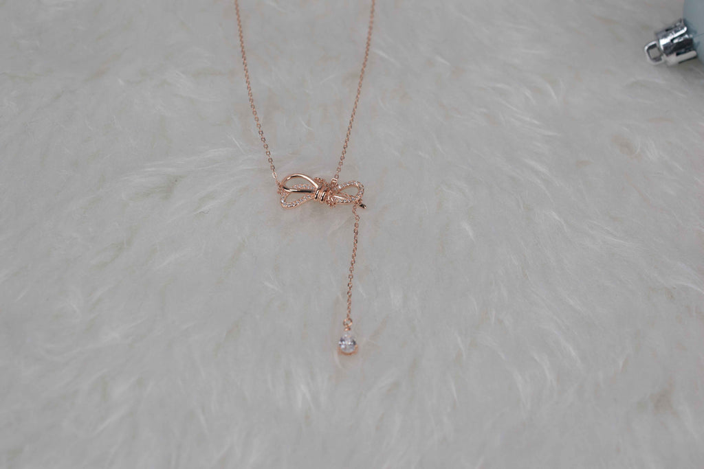 Collar con moña color oro rosa sobre superficie blanca