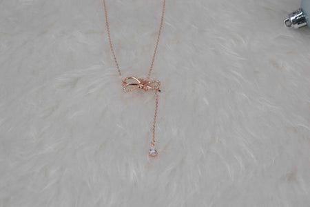 Collar con moña color oro rosa sobre superficie blanca