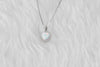 Detalle de collar en plata 925 y pendiente de ópalo sintético en forma de corazón y marco incrustado en zirconias
