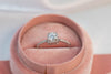 Anillo de plata 925 ajustable con zirconia central grande y zirconias pequeñas incrustadas en la banda exhibido dentro de caja de anillo rosa de frente