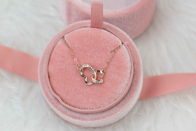 Collar con cadena y pendiente de corazones entrelazados formando una mariposa en baño oro rosa en caja de joyas rosa