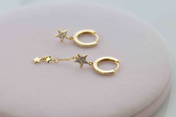 Aretes de plata 925 con baño de oro 18k en forma de argollas con estrellas colgantes y Zirconias exhibido sobre superficie blanca