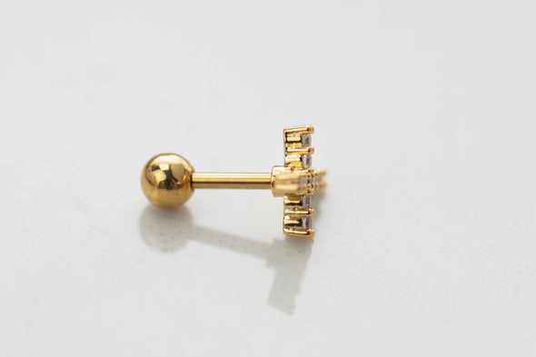 Detalle lateral de arete piercing de cruz color oro con cierre de esfera (bolita)
