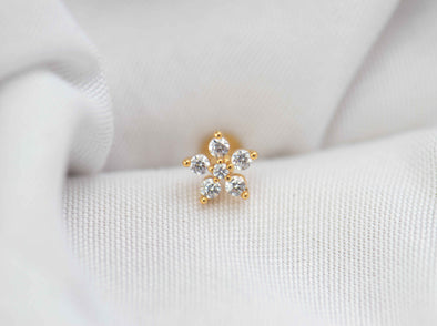 Detalle de arete piercing de flor color oro con piedras zirconias blancas
