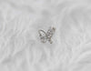 Arete piercing de mariposa color plata con zirconias blancas sobre tela blanca