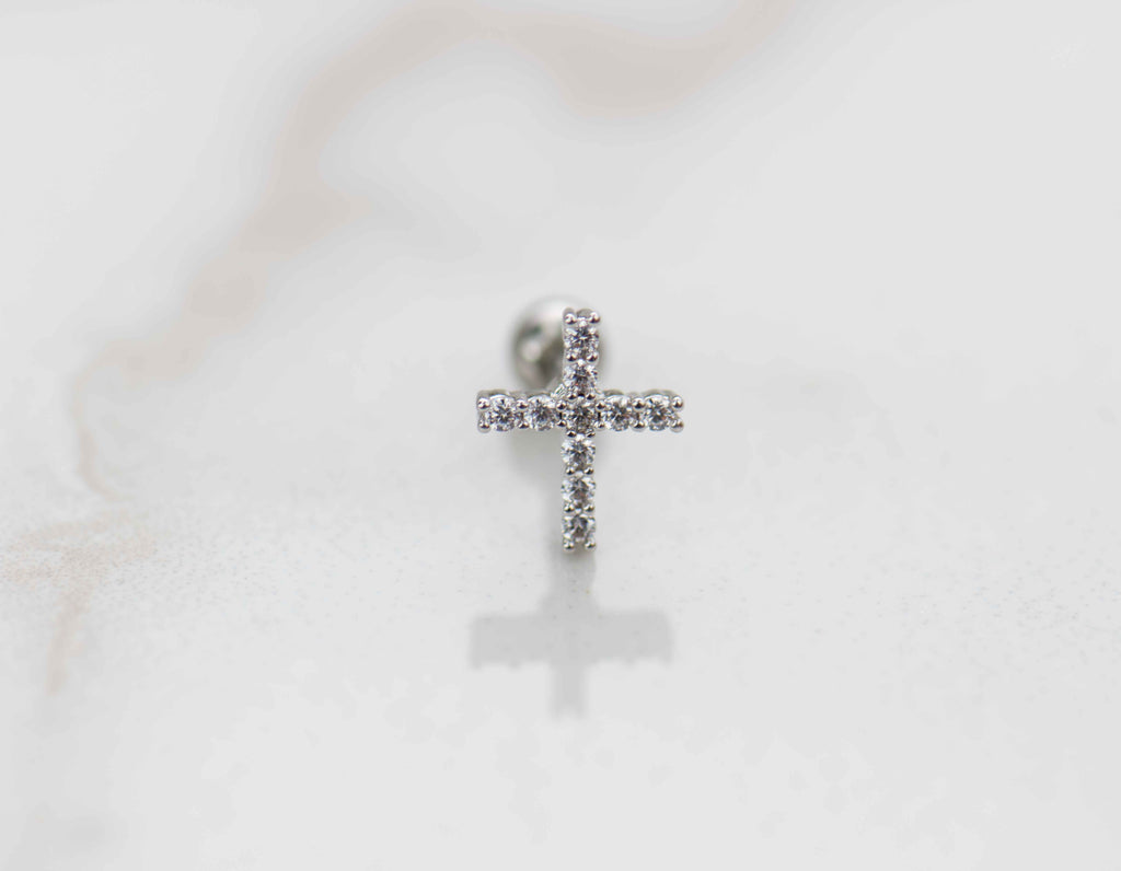 Detalle de arete piercing de cruz color plata con piedras zirconias blancas