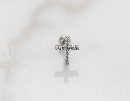Detalle de arete piercing de cruz color plata con piedras zirconias blancas
