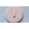 Collar de cadena color plata con pendiente de perla y zirconias incrustadas sobre superficie rosa