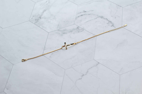 Pulera cadena delicada en color oro con cruz dorada extendida sobre superficie de mármol