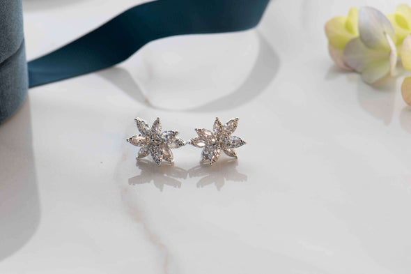 Aretes en sobre color plata con Flores de zirconias exhibidos sobre superficie blanca