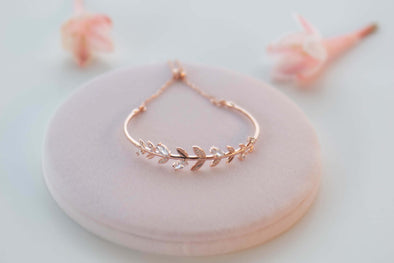 Brazalete con racimo de hojas en color oro rosa con zirconias blancas sobre superficie color rosa
