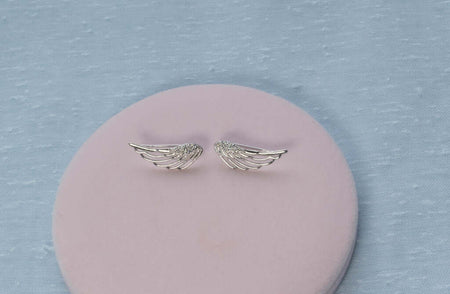 Aretes de plata 925 en forma de alas de ángel exhibidos sobre superficie rosa