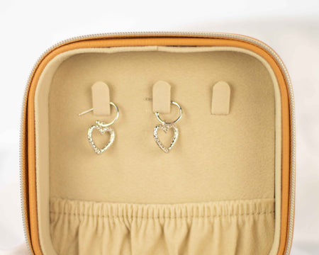 Aretes colgantes de corazón en plata 925 exhibidos en un joyero color beige de venta en Guatemala
