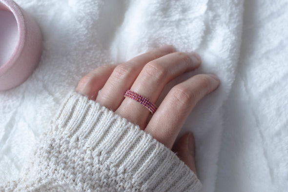 Mano usando anillo de plata 925 con baño de oro 18k y Zirconias color rosa exhibido sobre una superficie blanca