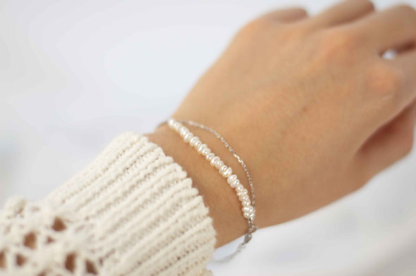 mano modelando pulsera color plata doble con cadena delicada y otra con piedras tipo perlas