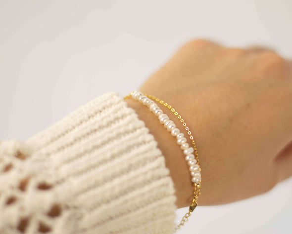 mano modelando pulsera color dorado doble con cadena delicada y otra con piedras tipo perlas