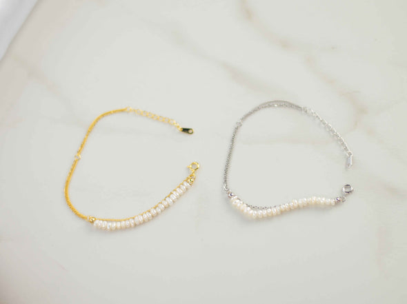 pulsera color plata doble con cadena delicada y otra con piedras tipo perlas y pulsera color dorado doble con cadena delicada y otra con piedras tipo perlas sobre superficie de mármol