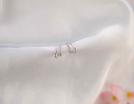 Par de aretes color plata con zirconias incrustadas blancas sobre seda blanca
