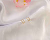 Par de aretes dorados con zirconias incrustadas blancas sobre seda blanca