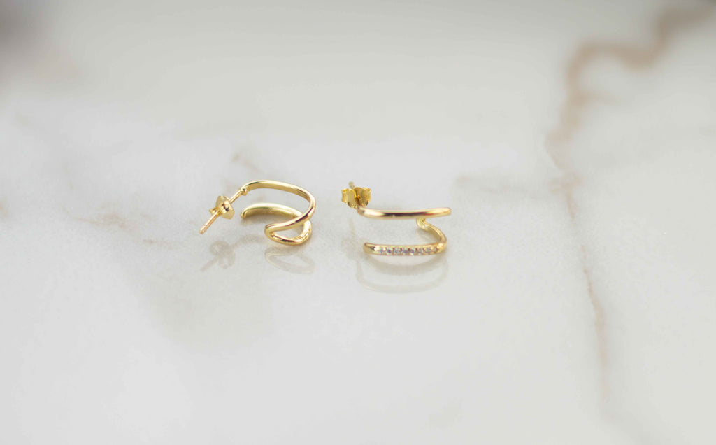 Par de aretes dorados con zirconias incrustadas blancas sobre superficie de mármol