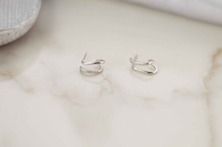 Par de aretes color plata con zirconias incrustadas blancas sobre superficie de mármol