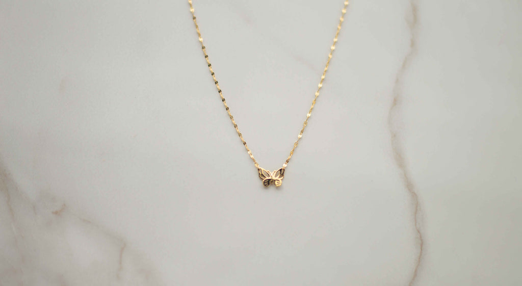 Collar de cadena dorada con mariposa dorada sobre superficie de mármol