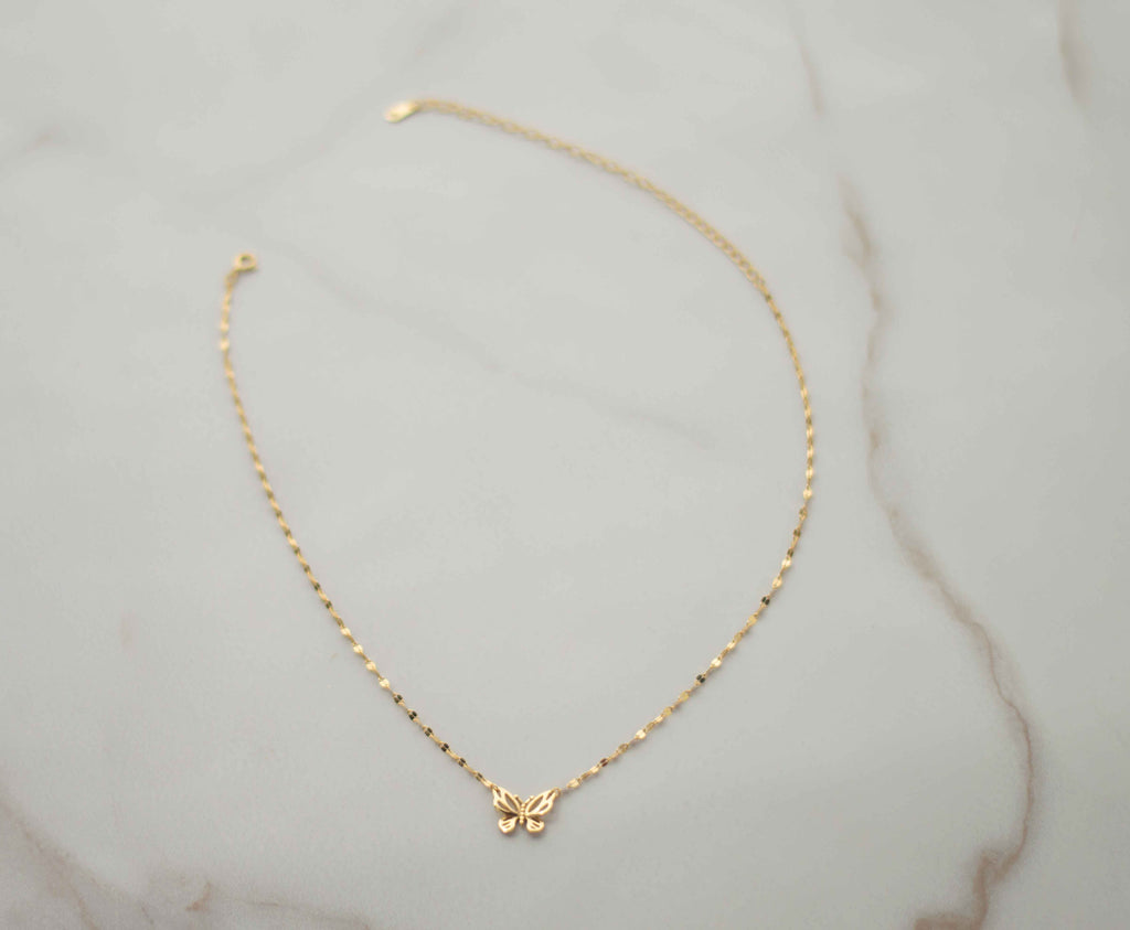 Collar de cadena dorada con mariposa dorada completo sobre superficie de mármol