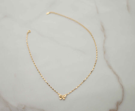 Collar de cadena dorada con mariposa dorada completo sobre superficie de mármol