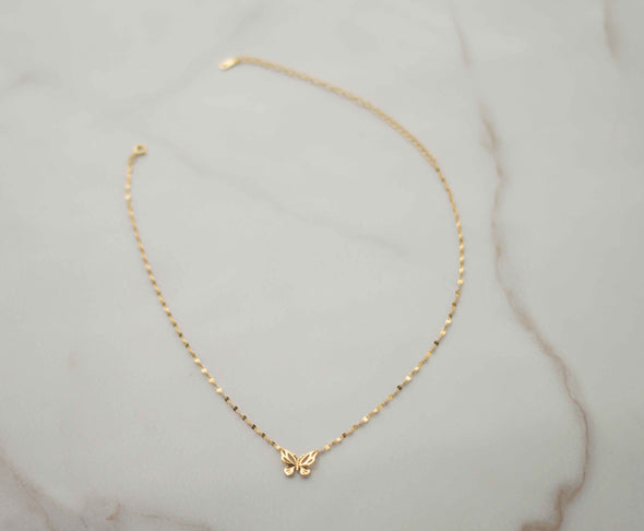 Collar de cadena dorada con mariposa dorada completo sobre superficie de mármol