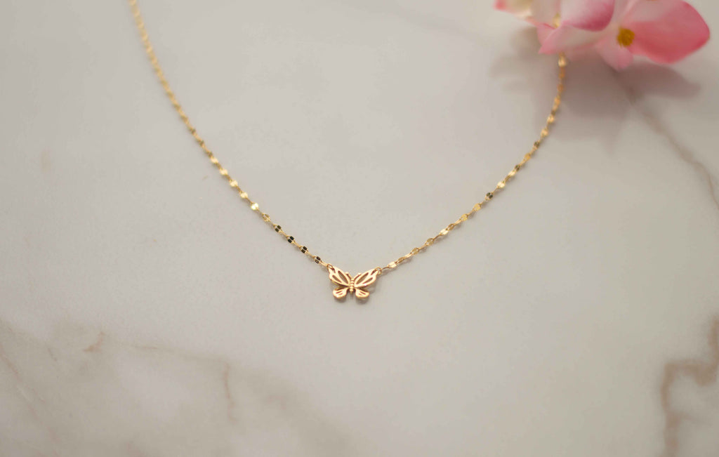 Collar de cadena dorada con mariposa dorada acercamiento sobre superficie de mármol