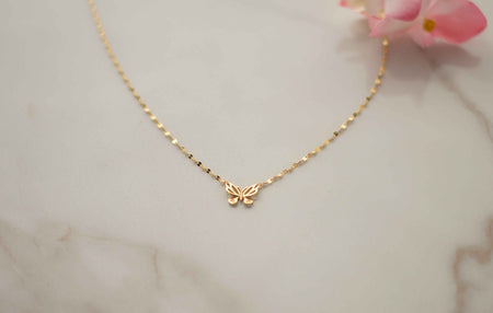 Collar de cadena dorada con mariposa dorada acercamiento sobre superficie de mármol