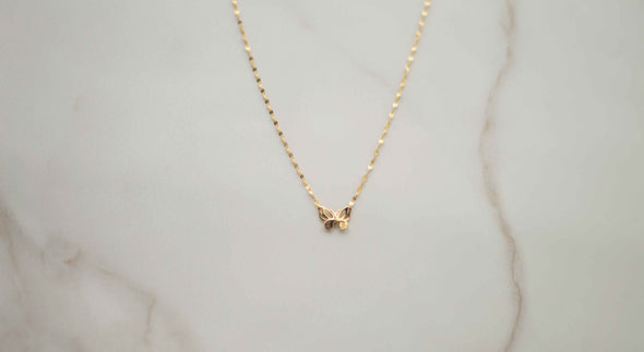 Collar de cadena dorada con mariposa dorada sobre superficie de mármol