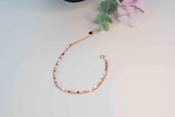 Pulsera doble color oro rosa con pequeños círculos y cadena sobre superficie blanca