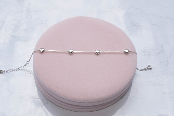 Pulsera con corazones en plata 925 sobre superficie rosa
