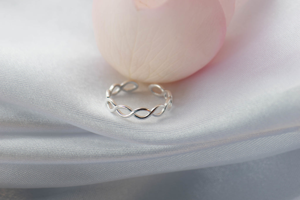Anillo de plata 925 trenzado con apertura para ajustar talla exhibido desde frente sobre seda blanca con pétalo rosa