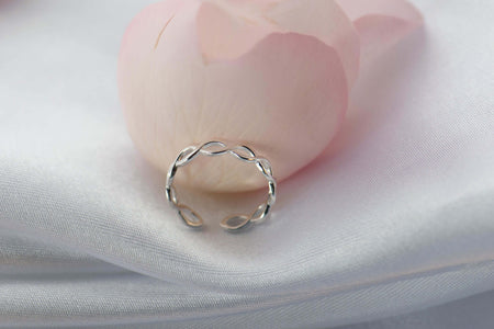 Anillo de plata 925 trenzado con apertura para ajustar talla exhibido sobre seda blanca con pétalo rosa