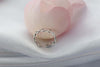 Anillo de plata 925 trenzado con apertura para ajustar talla exhibido sobre seda blanca con pétalo rosa